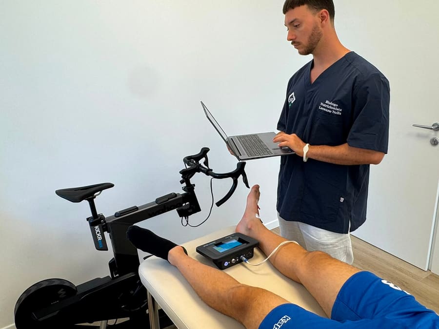 Bioimpedenziometria su un atleta nello studio di Lorenzo Nella, con smart trainer da ciclismo sullo sfondo.