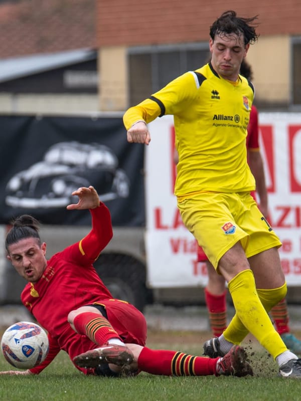 Contrasto di gioco durante una partita di calcio: un difensore in scivolata sul pallone contro un attaccante avversario.