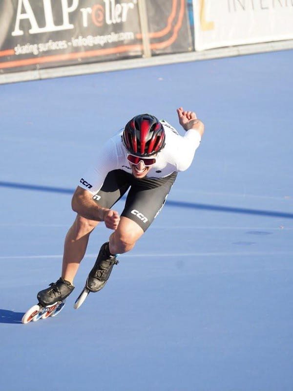 Pattinatore di velocità in linea in curva su pista blu durante una gara.